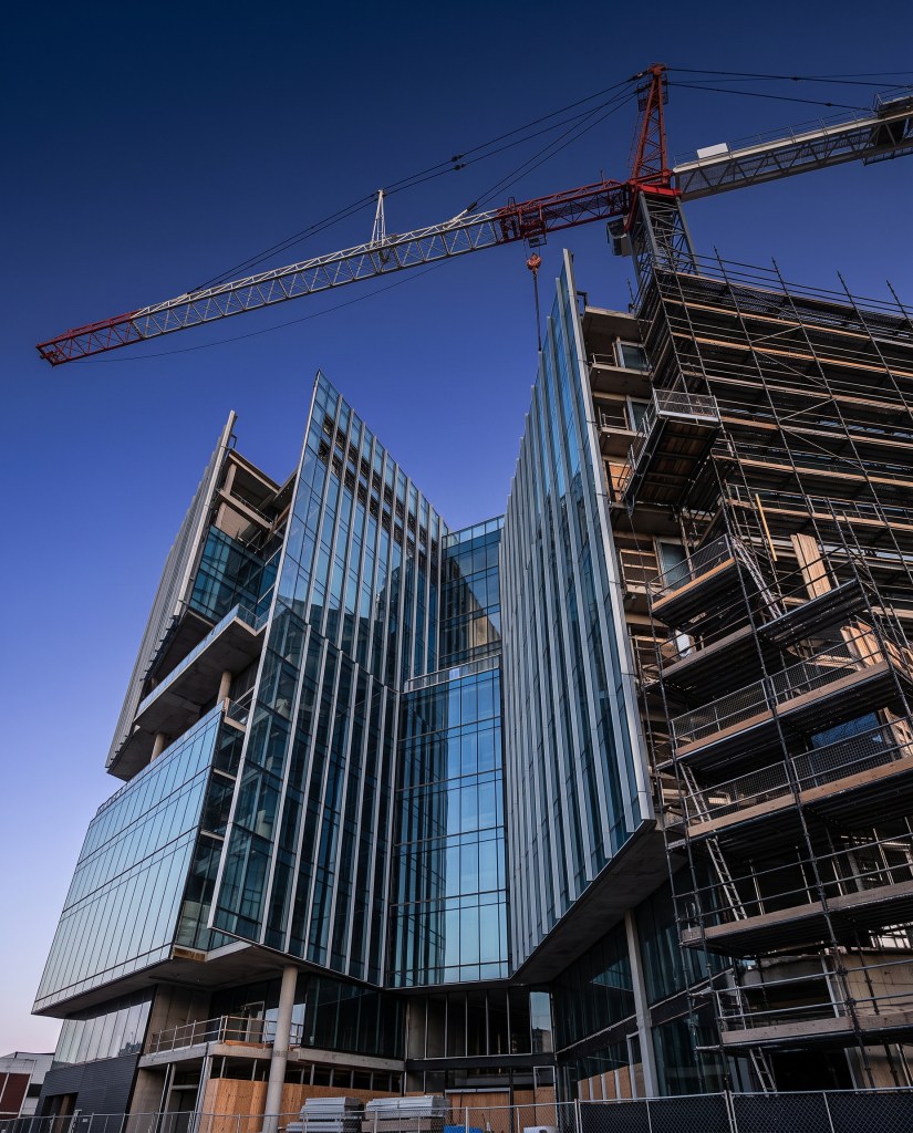 New glass office building nearing completion with scaffolding and a tower crane